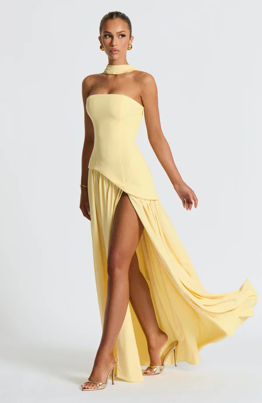 Woman wearing a yellow strapless gown with a slit on a white background