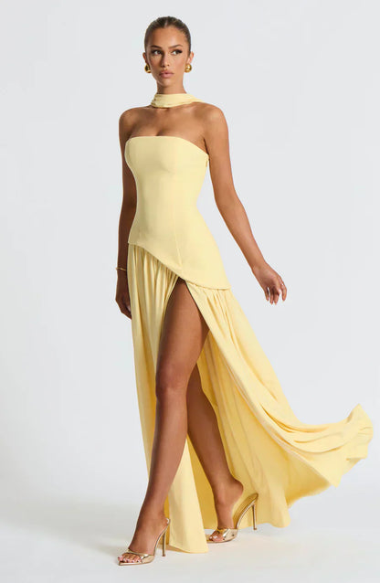 Woman wearing a yellow strapless gown with a slit on a white background