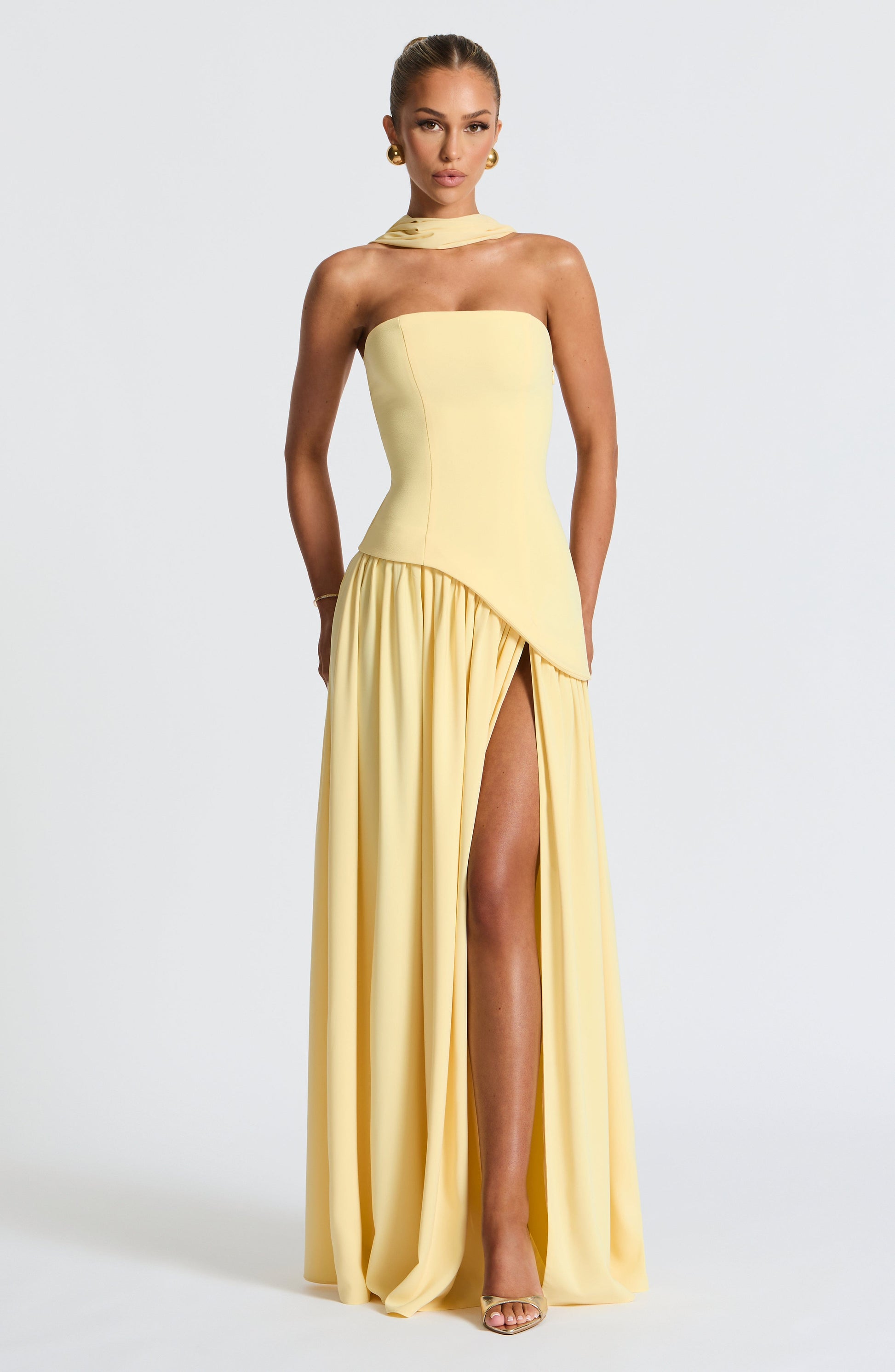 Woman wearing a yellow strapless gown with a slit on a white background